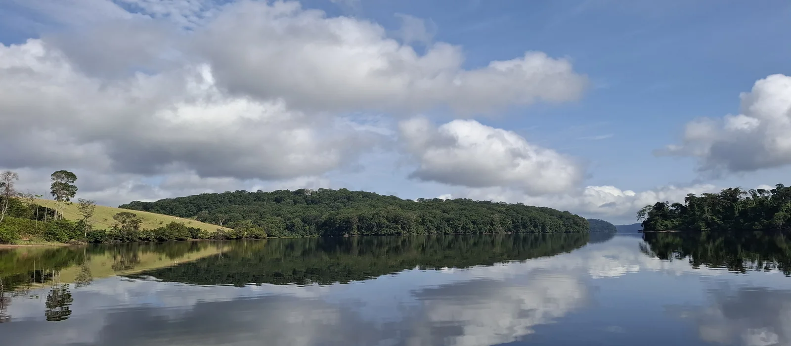 A forest river in Gabon, still enough to mirror the canopy and the clouds